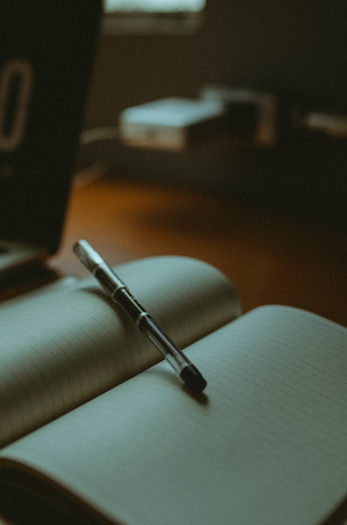 A stylish pen resting on an open lined notebook, set against a warm, blurred background.